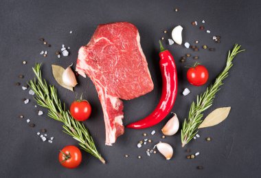 Baharatlı ve sebzeli çiğ biftek ve koyu beton masa arkaplanı. Kovboy bifteği ızgara için hazır.