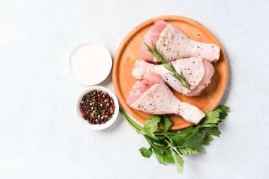 Baharatlı tavuk budu pişirmek ve ahşap tabakta beyaz masa arkasında baharat yemek. Çiğ tavuk bacağı pişmeye hazır. Organik et, sağlıklı yemek. 