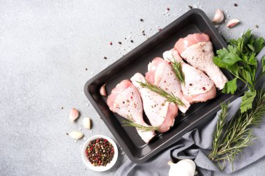 Raw chicken drumsticks in black baking form with seasonings over gray concrete table background. Chicken legs ready to cook. Organic meat, healthy eating