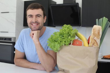 Mutfakta bir çanta dolusu taze sebzeli yakışıklı genç adamın portresi.