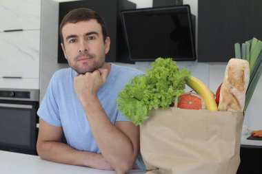 Mutfakta bir çanta dolusu taze sebzeli yakışıklı genç adamın portresi.