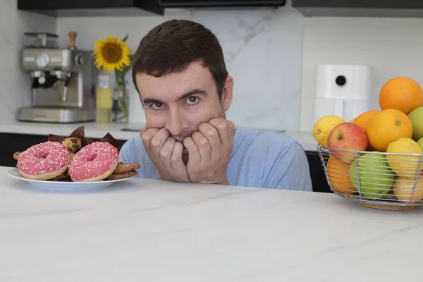 stock image portrait of handsome young man between fresh fruits and unhealthy pastry at kitchen