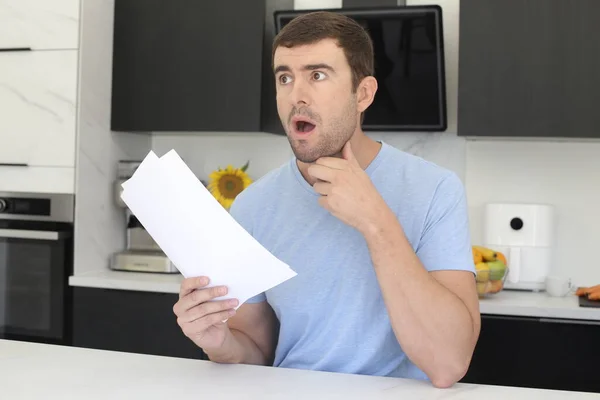 stock image portrait of handsome young man holding paper with shocked expression at kitchen