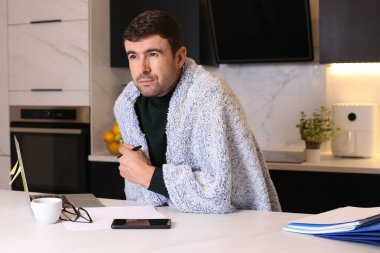 Mutfaktan çalışan, battaniyeli yakışıklı, hasta bir adamın portresi.