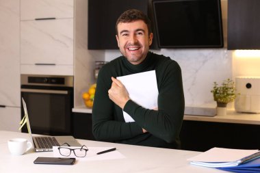 Mutfakta dizüstü bilgisayarla çalışan yakışıklı bir gencin portresi.