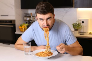 Mutfakta spagetti yiyen yakışıklı bir gencin portresi.