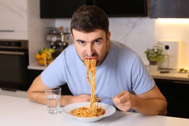 Mutfakta spagetti yiyen yakışıklı bir gencin portresi.