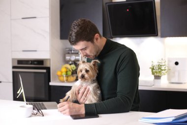 Mutfakta küçük sevimli köpeğiyle yakışıklı genç bir adamın portresi.