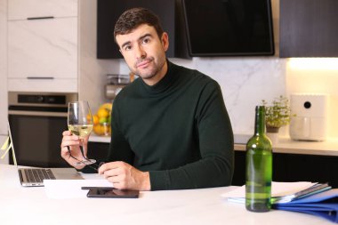 Bir bardak şarapla evde çalışan yakışıklı bir gencin portresi.