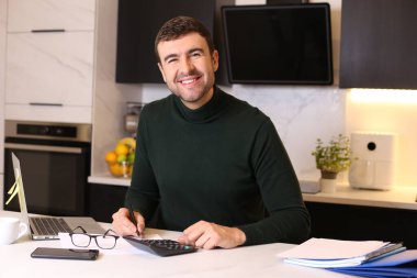 Mutfakta dizüstü bilgisayarla çalışan yakışıklı bir gencin portresi.