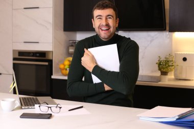 Mutfakta dizüstü bilgisayarla çalışan yakışıklı bir gencin portresi.