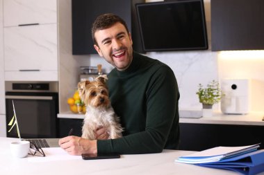 Mutfakta küçük sevimli köpeğiyle yakışıklı genç bir adamın portresi.