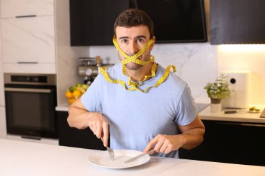 Kafası mutfakta mezura ile bağlanmış yakışıklı genç adam portresi, diyet konsepti.