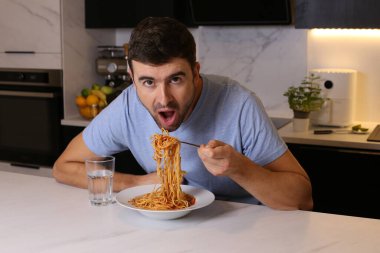 Mutfakta spagetti yiyen yakışıklı bir gencin portresi.