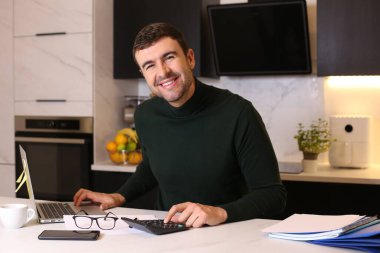 Mutfakta dizüstü bilgisayarla çalışan yakışıklı bir gencin portresi.