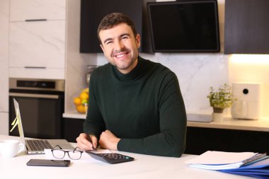 Mutfakta dizüstü bilgisayarla çalışan yakışıklı bir gencin portresi.