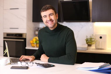 Mutfakta dizüstü bilgisayarla çalışan yakışıklı bir gencin portresi.