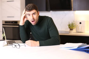 Mutfakta dizüstü bilgisayarla çalışan yakışıklı bir gencin portresi.