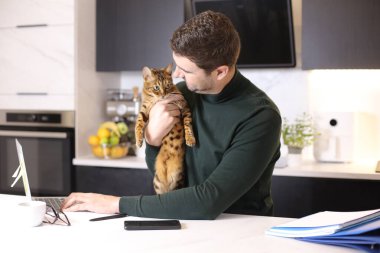 Yakışıklı ve egzotik kedisi mutfakta oturan genç adamın portresi.