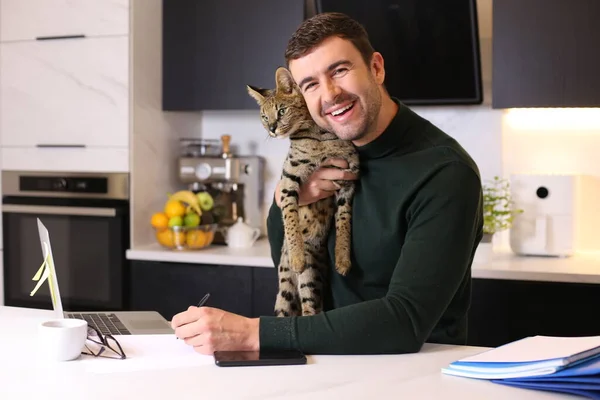 年轻英俊男子与他的异国情调的猫坐在厨房的肖像 — 图库照片
