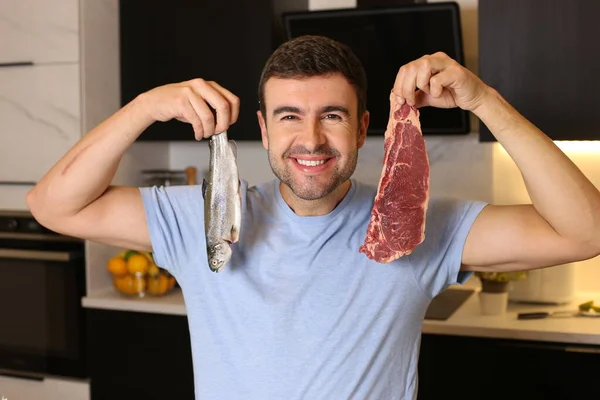 台所で肉や魚を持っているハンサムな若い男の肖像画 — ストック写真