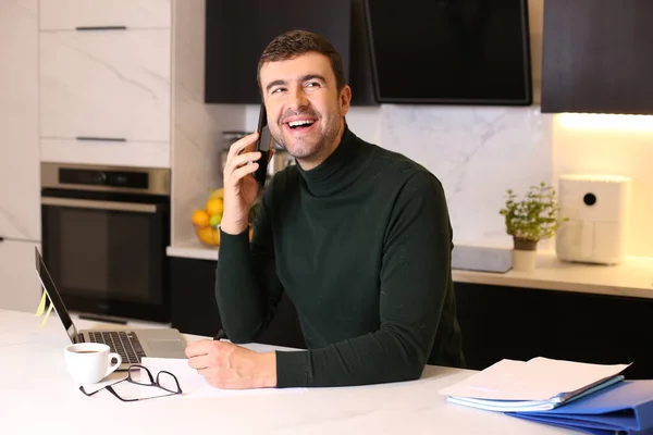 portrait of handsome young man talking by phone while working from home at kitchen