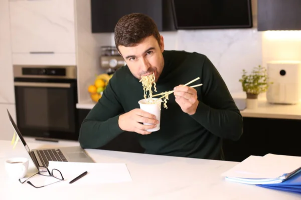 台所で自宅から仕事をしながらカップヌードルを食べるハンサムな若い男の肖像画 — ストック写真
