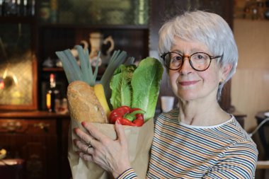 close-up portrait of mature woman with paper bag of groceries at home
