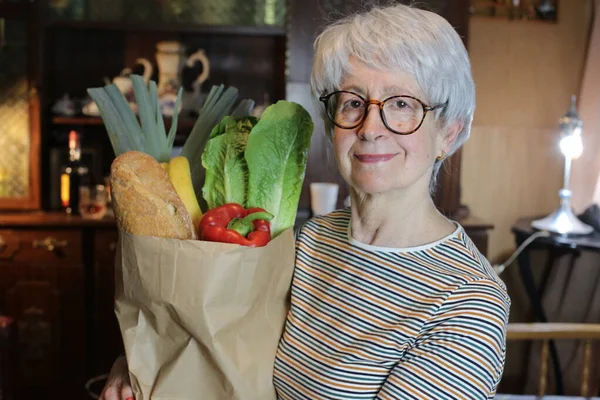 close-up portrait of mature woman with paper bag of groceries at home