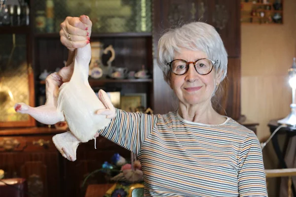 close-up portrait of mature woman with raw chicken at home