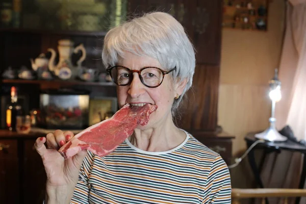 close-up portrait of mature woman with raw beef steak at home