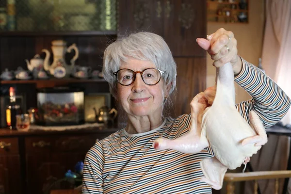 close-up portrait of mature woman with raw chicken at home