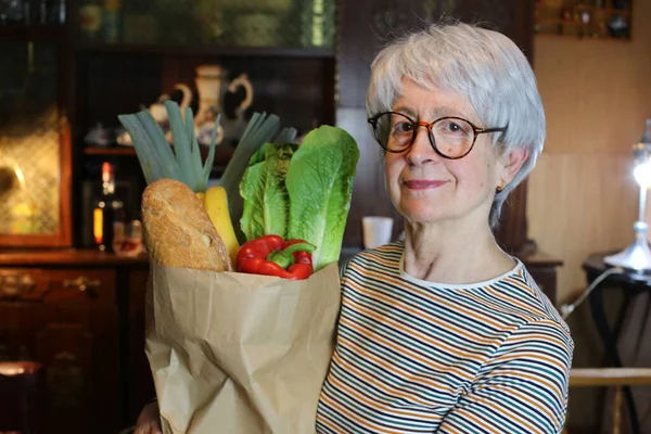 close-up portrait of mature woman with paper bag with groceries at home