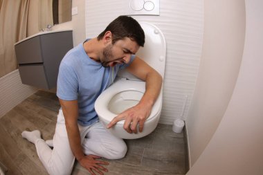 wide angle shot of young man vomiting in toilet