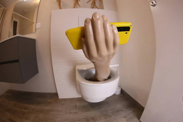 wide angle shot of hand with smartphone sticking out of toilet, comedy concept