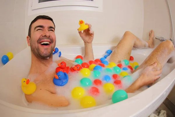 お風呂で楽しそうなゴム製のアヒルやボールを持つ幸せな若い男の広い角度ショット — ストック写真