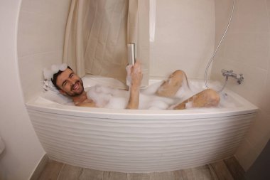 wide angle shot of handsome young man reading book in bath