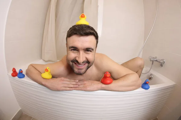 風呂の中でゴム製のアヒルとハンサムな若い男の広い角度ショット — ストック写真