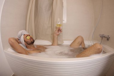 wide angle shot of handsome young man with glass of champagne in bath