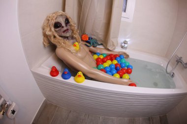 wide angle shot of mannequin with alien head in bath tub