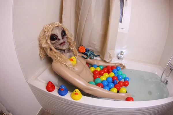 wide angle shot of mannequin with alien mask in bath tub