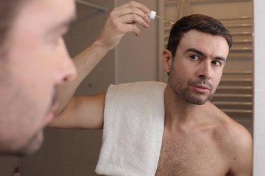 Yakışıklı genç adamın portresi banyoda aynanın önüne saç yağı sürüyor.