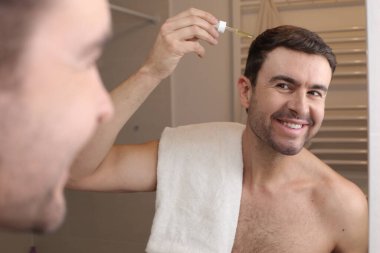 Yakışıklı genç adamın portresi banyoda aynanın önüne saç yağı sürüyor.