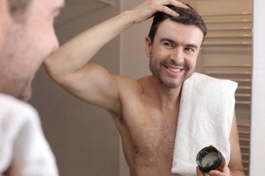 Yakışıklı bir gencin portresi banyoda aynanın önünde saç şekillendirme merhemi sürüyor.