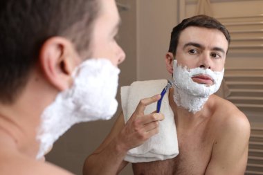 Banyoda aynanın önünde tıraş olan yakışıklı bir gencin portresi.