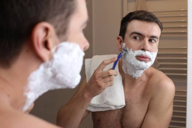 Banyoda aynanın önünde tıraş olan yakışıklı bir gencin portresi.