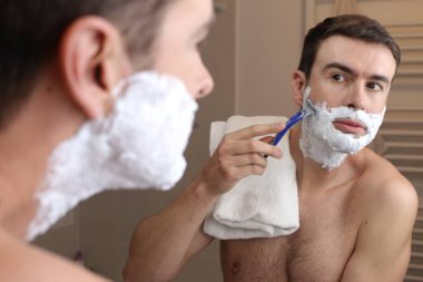 Banyoda aynanın önünde tıraş olan yakışıklı bir gencin portresi.