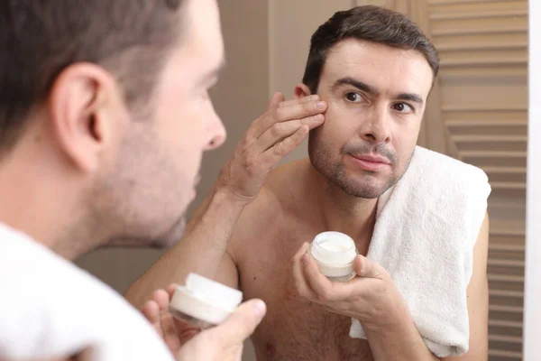 stock image portrait of handsome young man applying facial cream in front of mirror in bathroom