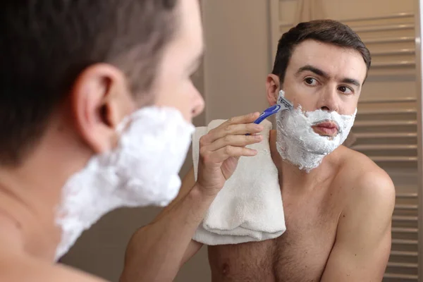 年轻英俊男子在浴室镜子前刮胡子的肖像 — 图库照片