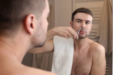 Banyoda aynanın önünde burun kıllarını kesen yakışıklı bir gencin portresi.